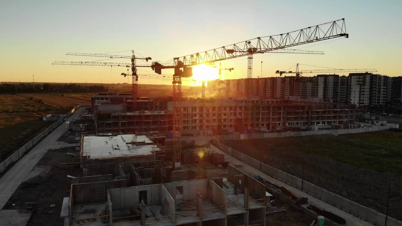 Tower cranes silhouetted over a construction site at sunset